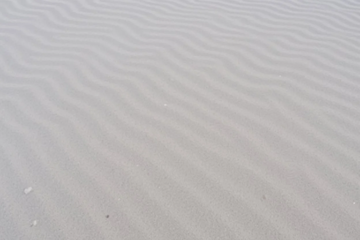 wavy rippled beach sand, lighter in top left, dark in bottom right