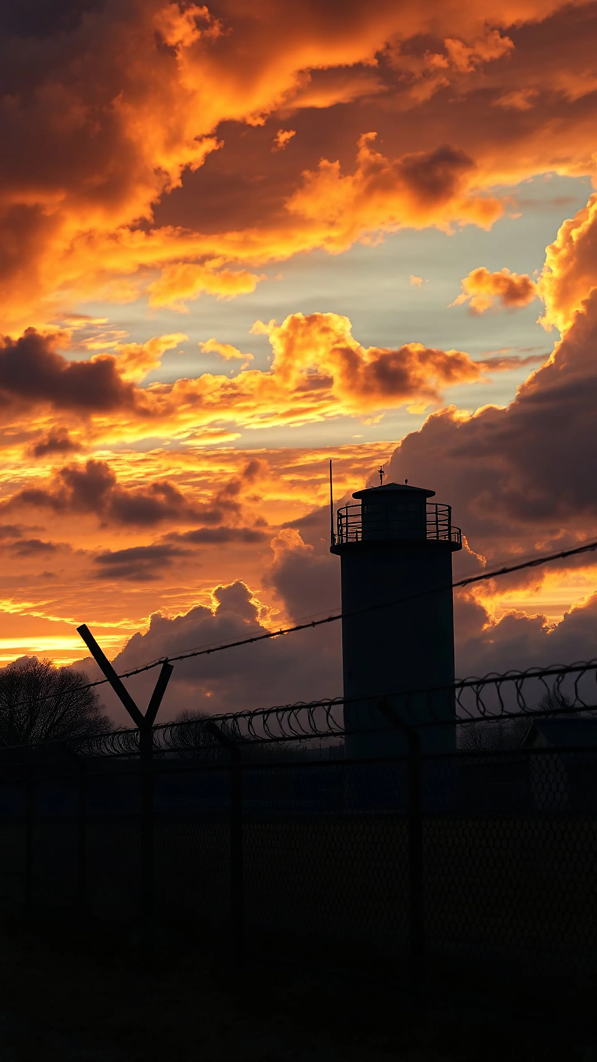 sunset,Dramatic Clouds s prison with gardd tower and prisoners try to escape Behind A Barbed Wire Fence