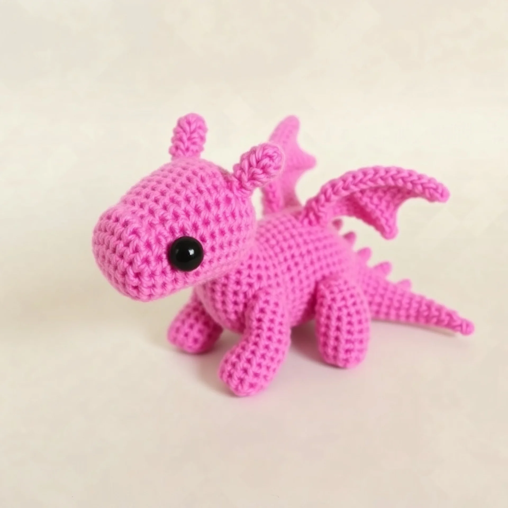 Generate a big pink crochet dragon, with black safety eyes.