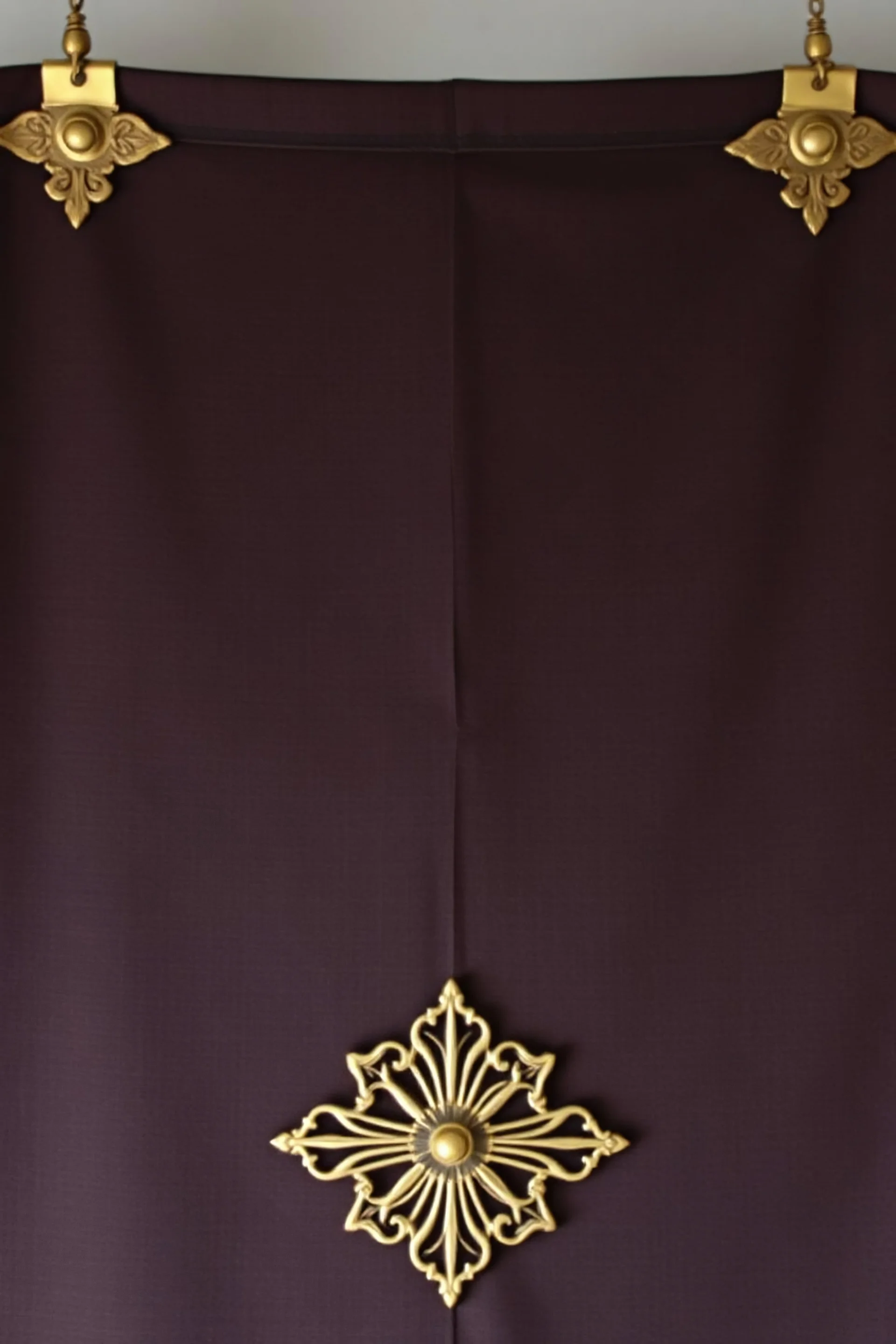 darker textured hanging fabric background with decorative brass corners at top, and a wide brass decorative element clamped across the bottom