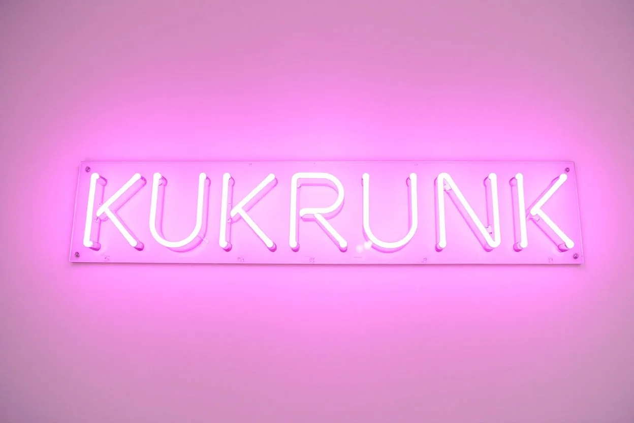 A simple neon sign labeled "KUKRUNK" white background and bold 80s font