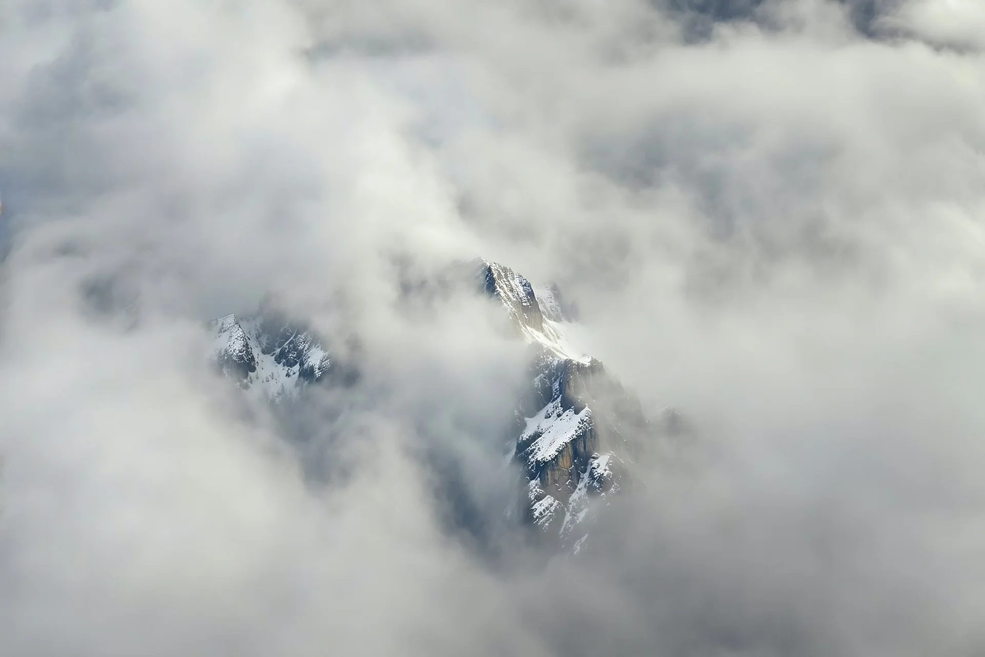 a massive sheer snowy mountain cliff with very sparse vegetation scaling vertically into the sky, partially obscured by dense clouds(color d0d1d5) and mist. the borders — top, bottom, left, and right — fade smoothly into thick fog, while the center reveals the steep, rocky cliff face with fine texture and detail. atmospheric lighting, cinematic composition, natural colors, high contrast between fog and stone. photography
