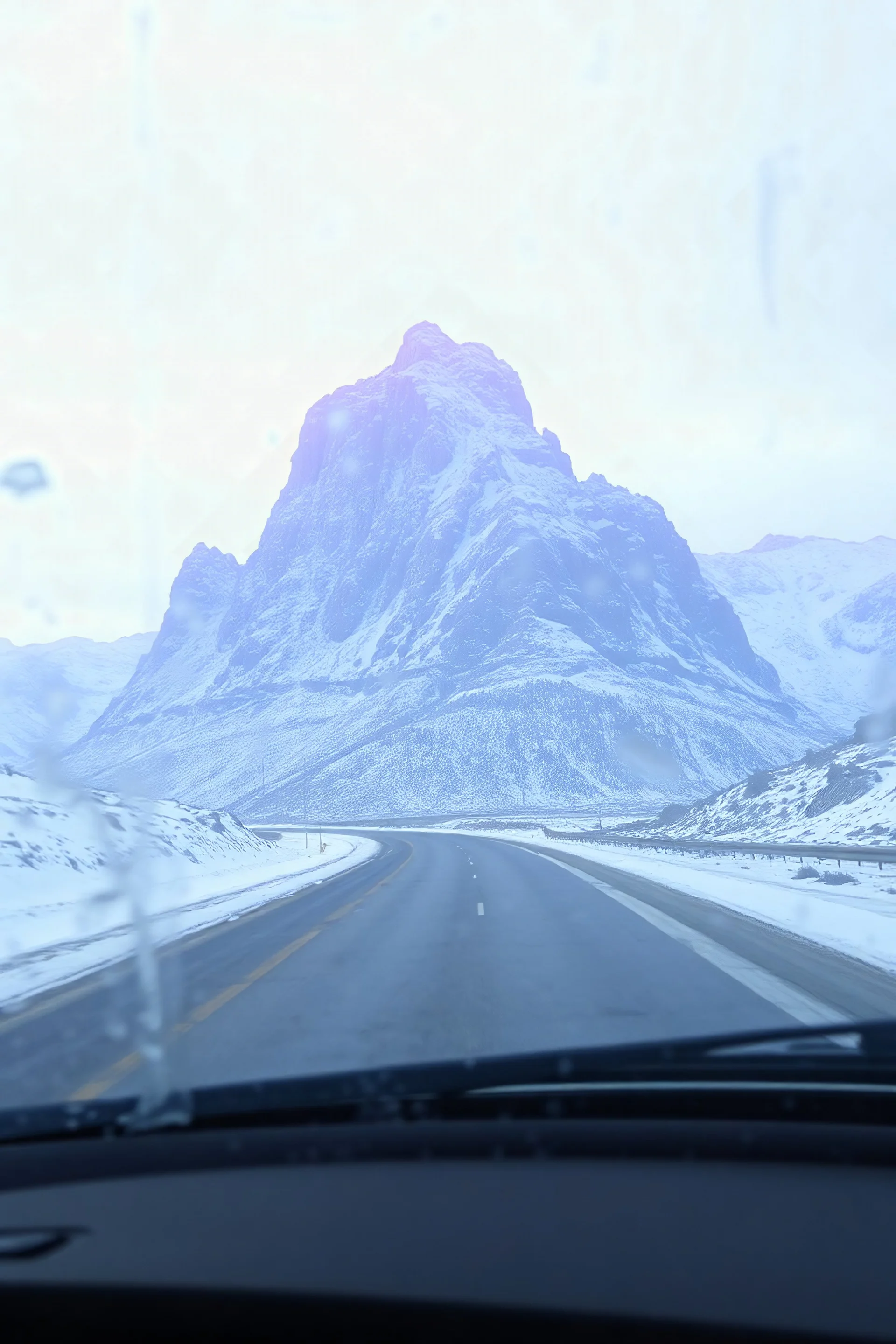 surreal purple plastic mountain road seen through a dirty truck front window, dirty blue snow and wind