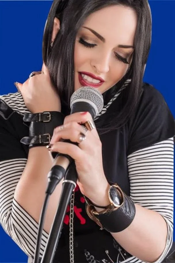 attractive female country music singer leaning forward while holding microphone in one hand, other hand brought up to side of neck, change clothing to plaid in natural tones, leather bracelets on wrists, long hair, mouth open singing, rings on fingers, eyes closed