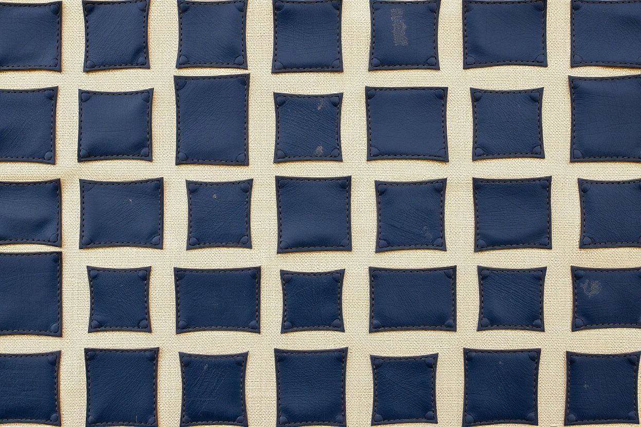 canvas background covered with a grid of many irregular rectangular weathered navy blue leather patches that are each stitched around the edges