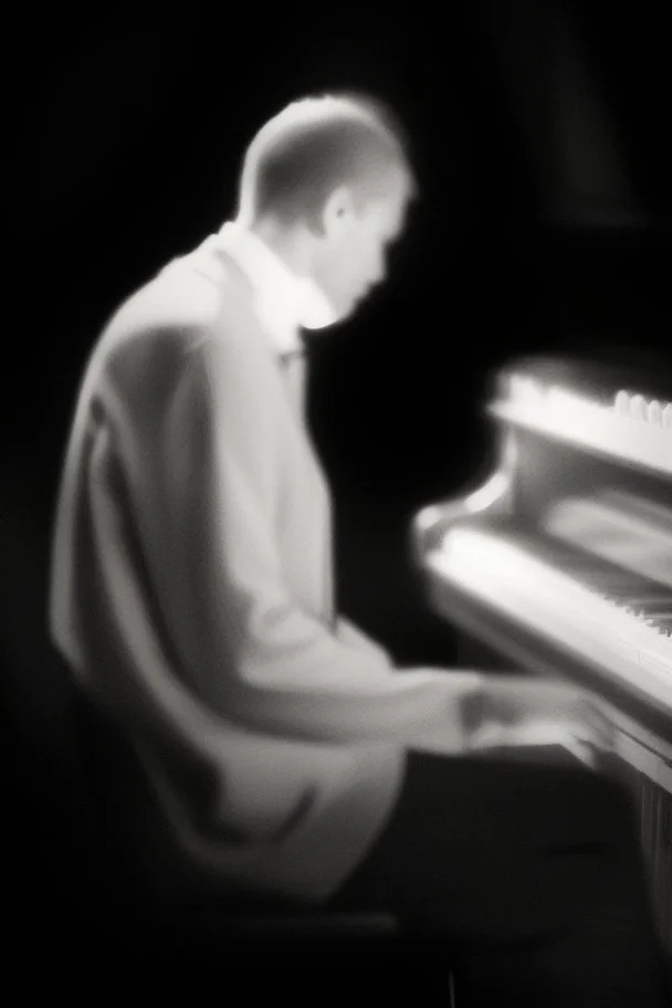Hombre, pianista, tocando el piano, mirando hacia su derecha, fuertemente iluminado desde, blanco y negro vaporoso, al estilo del fotógrafo Hugo Alonso