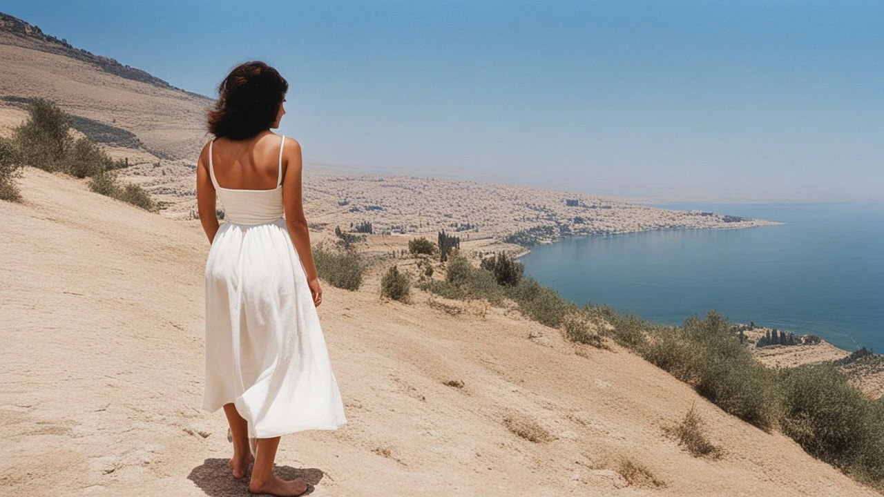 [photo by Russ Meyer] close to the old town of Nazareth, a view on the Lake of Genesareth. a young woman in linen dress, she has her wooden rod she looks at the people down around the shore