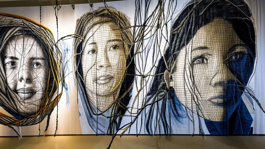 Using your 3 portrait as the centerpiece, create a large-scale fabric mural. Surround the portrait with a network of resilient and stretchy threads, symbolizing the challenges faced during addiction and the journey to recovery. Visitors can interact by gently tugging on the threads, emphasizing the importance of resilience in the healing process.