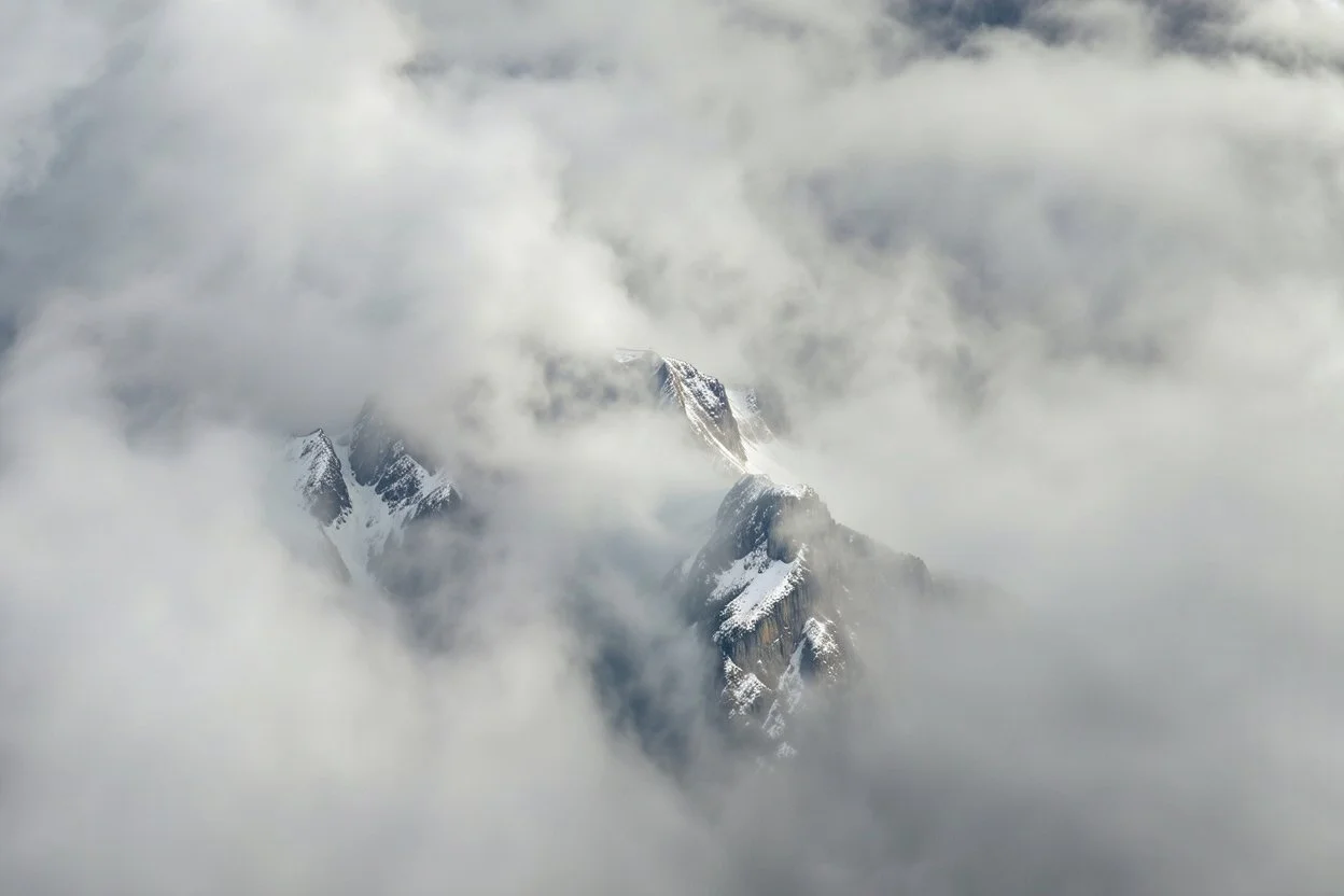 large scale, far away. a massive sheer snowy mountain cliff with very sparse vegetation scaling vertically into the sky, partially obscured by dense clouds(color d0d1d5) and mist. the borders — top, bottom, left, and right — fade smoothly into thick fog, while the center reveals the steep, far away rocky cliff face with fine texture and detail. atmospheric lighting, cinematic composition, natural colors, high contrast between fog and stone. photography