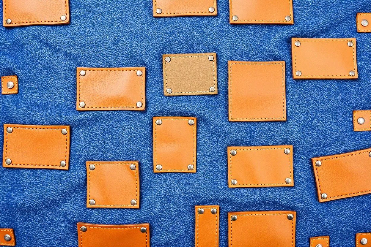 blue denim background covered with a grid of many rectangular tan leather patches that are each stitched around the edges