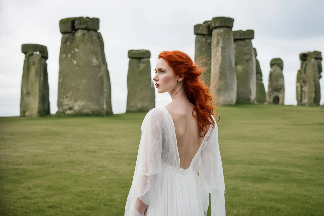 A tall slim red-headed woman, in a white floaty dress, standing in front of Stonehenge