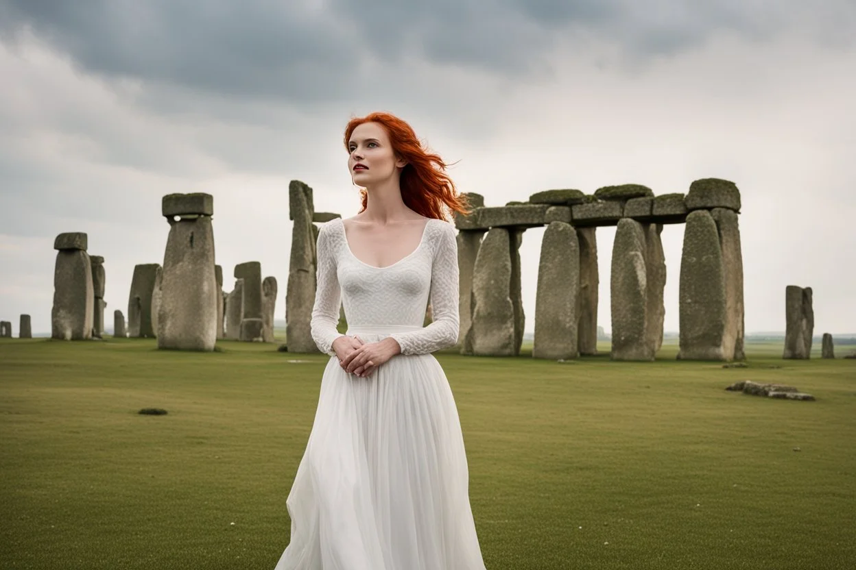 A tall slim red-headed woman, in a white floaty dress, standing in front of Stonehenge