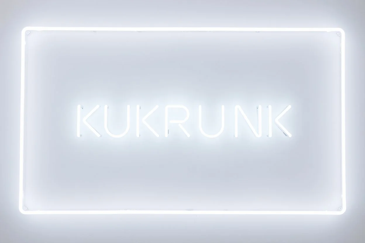 A simple neon sign labeled "KUKRUNK" white background and bold 80s font