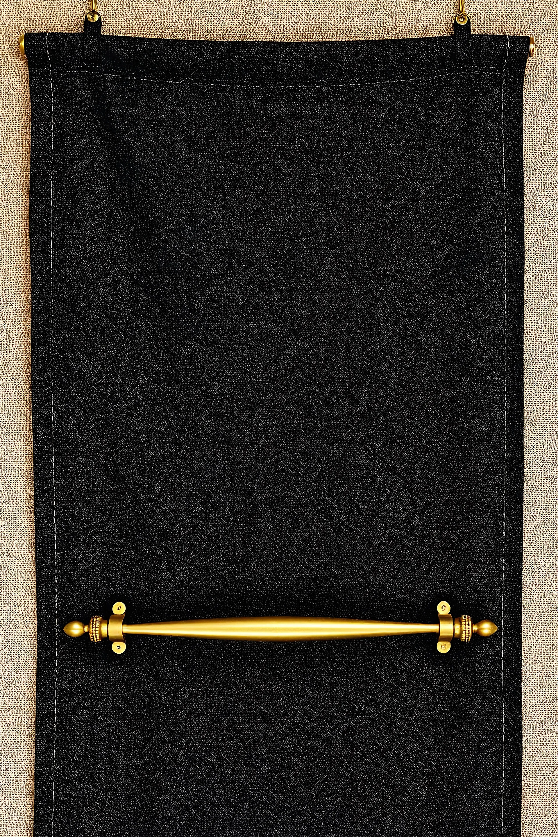 darker textured hanging fabric background with decorative brass corners at top, and a wide decorative brass bar clamped across the bottom