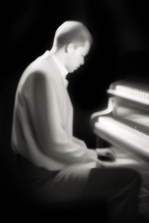 Hombre, pianista, tocando el piano, mirando hacia su derecha, fuertemente iluminado desde, blanco y negro vaporoso, al estilo del fotógrafo Hugo Alonso