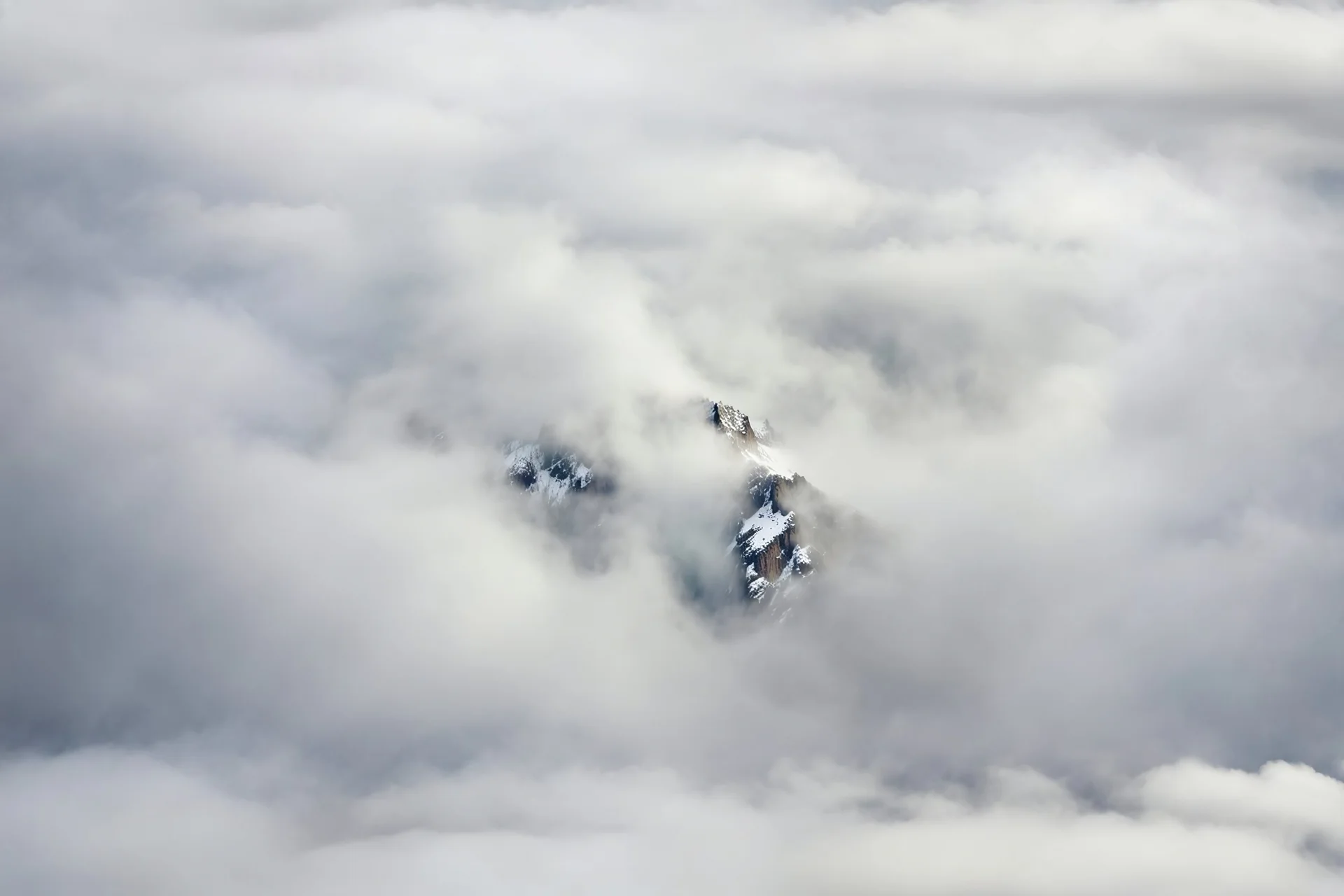 large scale, far away. a massive sheer snowy mountain cliff with very sparse vegetation scaling vertically into the sky, partially obscured by dense clouds(color d0d1d5) and mist. the borders — top, bottom, left, and right — fade smoothly into thick fog, while the center reveals the steep, far away rocky cliff face with fine texture and detail. atmospheric lighting, cinematic composition, natural colors, high contrast between fog and stone. photography