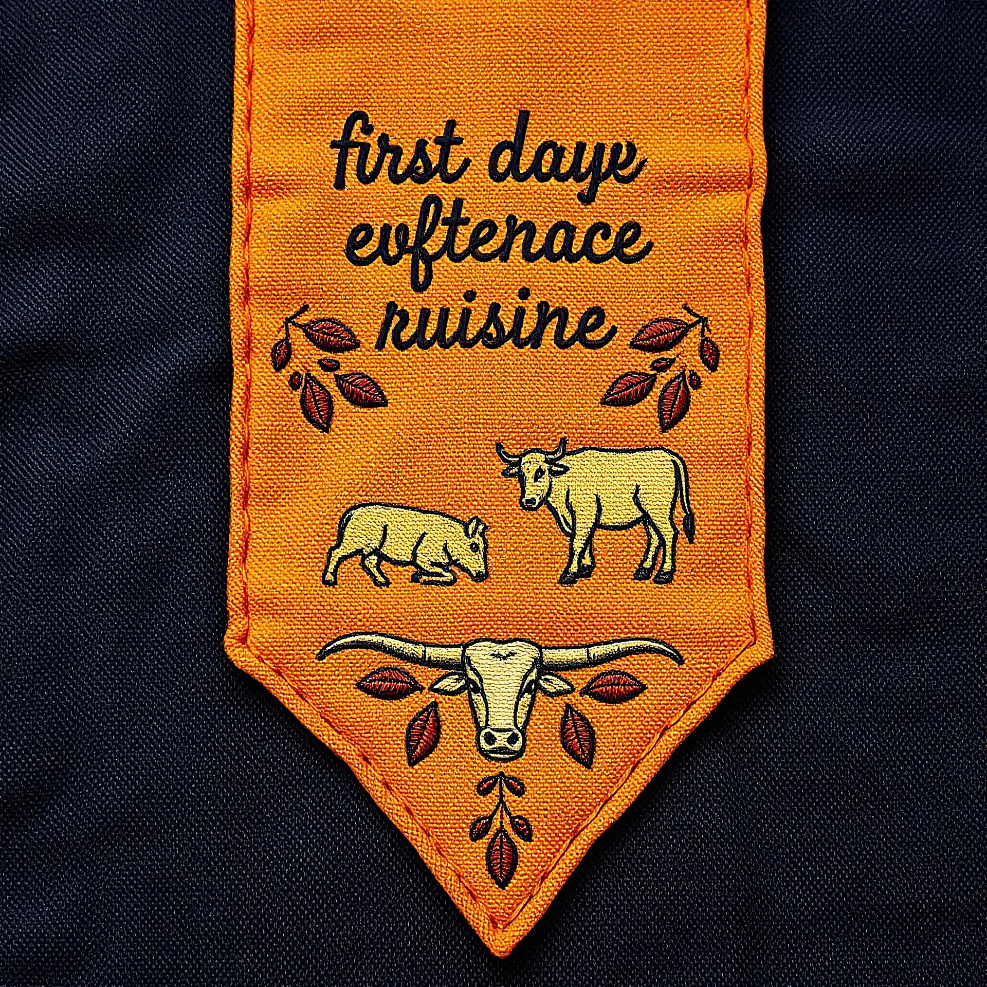 an autumn colored textured cloth embroidered with ornamental leaves and cattle, pointed bottom, on darker textile background, embroidered text across top, western textile art design