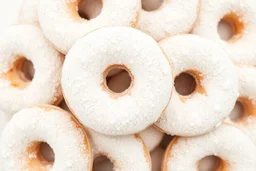 A close-up image of a pile of powdered sugar donuts, with the donuts overlapping and the powdered sugar coating them evenly. The background should be white or a light neutral color.