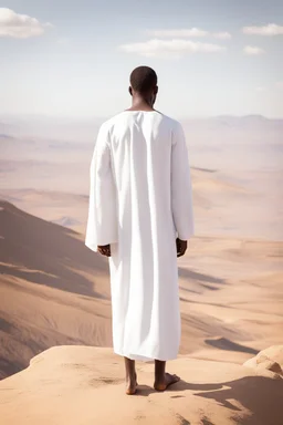 african man wearing white thobe. standing on high mountain looking out to the desert