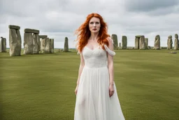 A tall slim red-headed woman, in a white floaty dress, standing in front of Stonehenge