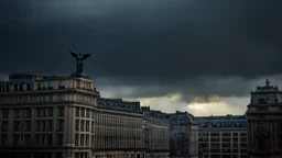 Dramatic, moody cityscape photograph featuring a row of tall, historic buildings under a dark, stormy sky. The layout is vertical, with the buildings aligned in a perspective that leads the eye towards the horizon. The architecture is characterized by a mix of classical and early 20th-century styles, with ornate facades and intricate details. A prominent feature is a statue of an angel atop one of the buildings, illuminated by a beam of sunlight breaking through the clouds. The buildings are pre