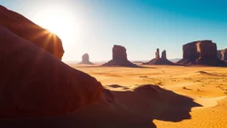 The foreground is dominated by a massive, sunlit rock formation that casts a deep shadow across the sandy terrain. The rock's surface is textured, with reddish-brown hues accentuated by the sunlight. In the distance, a series of tall, slender sandstone monoliths rise from the desert floor, adding a sense of depth and perspective to the scene. The arid landscape is bathed in the warm hues of sand, while the sky is clear, brilliant blue, devoid of clouds, suggesting ornate, dry weather. The high c