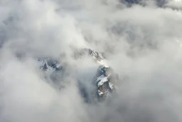 a massive sheer snowy mountain cliff with very sparse vegetation scaling vertically into the sky, partially obscured by dense clouds(color d0d1d5) and mist. the borders — top, bottom, left, and right — fade smoothly into thick fog, while the center reveals the steep, far away rocky cliff face with fine texture and detail. atmospheric lighting, cinematic composition, natural colors, high contrast between fog and stone. photography