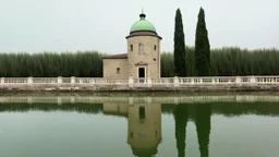 An ancient, weathered stone building with a green domed roof stands tall in the center of the image, reflected perfectly in the still, calm water below. A delicate white balustrade extends from the side of the building, also mirrored in the water. The building is surrounded by a lush, green treeline and tall, slender cypress trees on the horizon. The sky is overcast with soft, muted colors, contributing to the serene and timeless atmosphere of the painting. The overall style is realistic with a