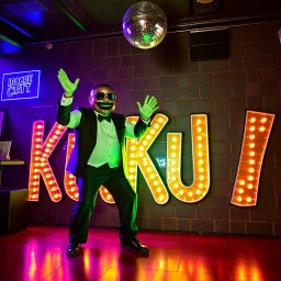 MR Kukrunk is Benny and DJ Roy in a disco, dancing, "Kukrunk" on sign wall, disco light, strobe, disco ball