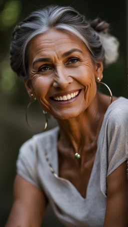 Portrait of a 60 year old Olive skinned woman with greying hair tied up in a bun, smiling