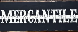fill composition with large and wide hand painted old western sign that reads: "MERCANTILE" white on black with inset white stripe aged paint on wood sanserif