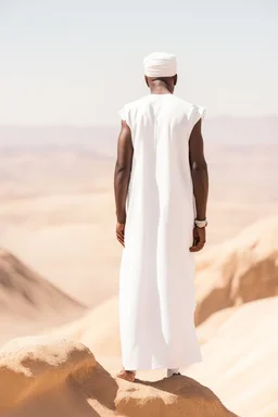 african man wearing white thobe. standing on high mountain looking out to the desert