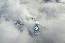 a massive sheer snowy mountain cliff with very sparse vegetation scaling vertically into the sky, partially obscured by dense clouds(color d0d1d5) and mist. the borders — top, bottom, left, and right — fade smoothly into thick fog, while the center reveals the steep, rocky cliff face with fine texture and detail. atmospheric lighting, cinematic composition, natural colors, high contrast between fog and stone. photography