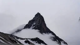 looking up at a single sharp narrow mountain, the peak obscured by clouds and fog.