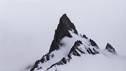looking up at a single sharp narrow mountain, the peak covered by clouds and fog.