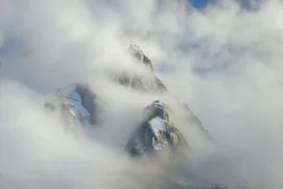 large scale, far away. a massive sheer snowy mountain cliff with very sparse vegetation scaling vertically into the sky, partially obscured by dense clouds(color d0d1d5) and mist. the borders — top, bottom, left, and right — fade smoothly into thick fog, while the center reveals the steep, far away rocky cliff face with fine texture and detail. atmospheric lighting, cinematic composition, natural colors, high contrast between fog and stone. photography