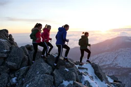 a group of Turkish young ladys in sports pants and blouse winter jacket are climbing over a rock mountain ,cloudy sun set sky,snowy environment