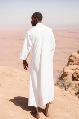 african man wearing white thobe. standing on high mountain looking out to the desert