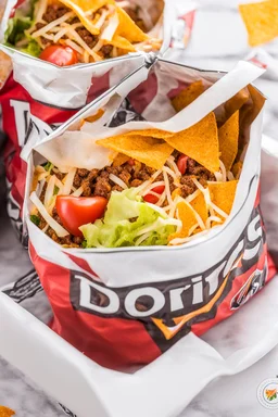 "Taco in a Bag" which consists of an open Doritos chip bag with sides rolled down, containing Doritos chips and cooked ground beef and lettuce and shredded cheese and chopped tomato pepper and onions and topped with more nacho chips, food blogger photography