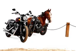 a motorcycle(harley davidson pan america 1250) next to a different motorcycle(Indian Springfield Dark Horse) next to a horse tied to a wood railing. white background. dirt ground. silkscreen image