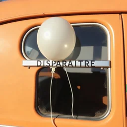 ballon fondu par le soleil, à la vitre d'une voiture vintage, avec le mot français "DISPARAITRE" sur la vitre