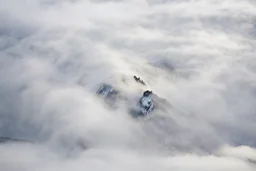 large scale, far away. a massive sheer snowy mountain cliff with very sparse vegetation scaling vertically into the sky, partially obscured by dense clouds(color d0d1d5) and mist. the borders — top, bottom, left, and right — fade smoothly into thick fog, while the center reveals the steep, far away rocky cliff face with fine texture and detail. atmospheric lighting, cinematic composition, natural colors, high contrast between fog and stone. photography