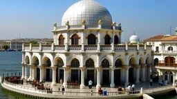 A white Mediterranean-style building with domed roofs and balconies overlooking a body of water, with people sitting on the balcony and boats in the foreground