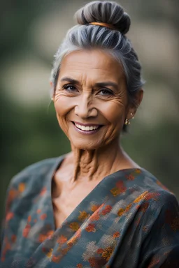 Portrait of a 60 year old Olive skinned woman with greying hair tied up in a bun, smiling