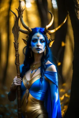 A picture of a beautiful blue faced indian goddess with skin painted blue, blue painted body, blue painted torso, wild black hair, stag antlers, elven ears, golden skirt, holding a staff in a sunny forrest