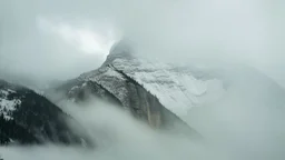 a massive sheer snowy mountain cliff with very sparse vegetation scaling vertically into the sky, partially obscured by dense clouds and mist. the borders — top, bottom, left, and right — fade smoothly into thick fog, while the center reveals the steep, rocky cliff face with fine texture and detail. atmospheric lighting, cinematic composition, natural colors, high contrast between fog and stone.