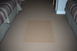 motel room floor, worn carpet with a faint rectangular discoloration where furniture used to be, uneven lighting, harsh flash photography, poorly framed, candid documentary photo, no clear subject