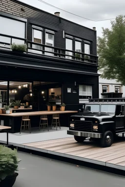 Foto van een vrachtwagen omgebouwd naar modern hip groot rijdend buurthuis (restaurant) zwart tafeltjes buiten er omheen.