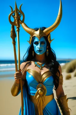 A picture of a blue faced Indian goddess with skin painted blue, wild black hair, stag horn antlers, elven ears, golden skirt, holding a staff on a sunny beach