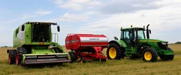 Parked at the edge of a field is a Claas brand Combine(left) Vaderstad Seeder(middle, red) and a John Deere Tractor(right) simplified